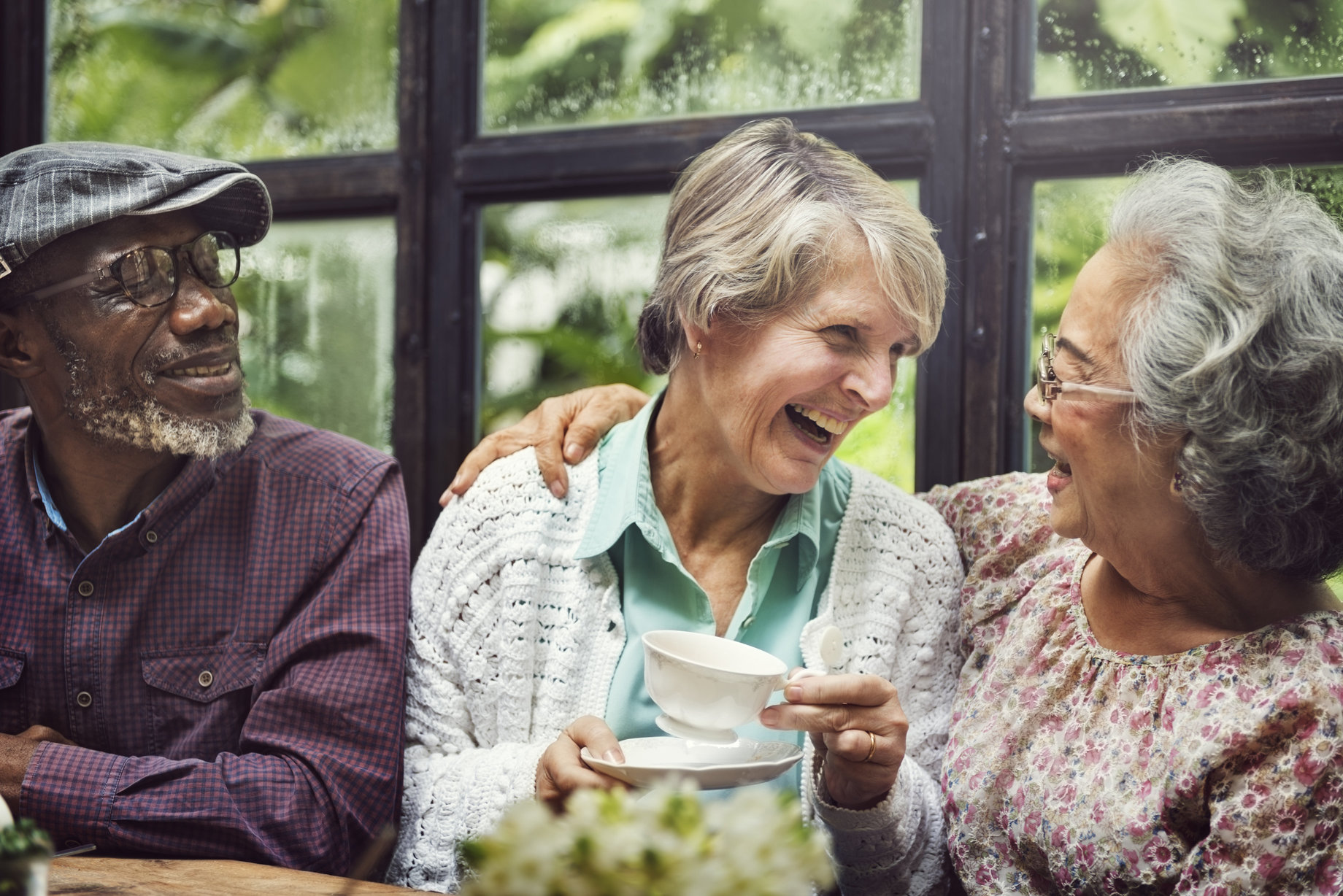 Three older adult friends laughing while sitting down at a table